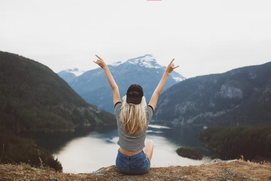 Girl sitting on a mountain with hands raised