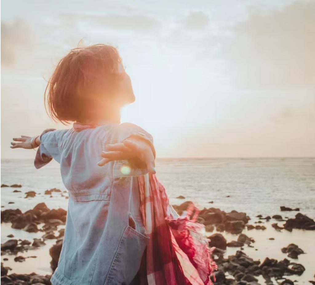 Girl with outstretched arms looking out over the ocean