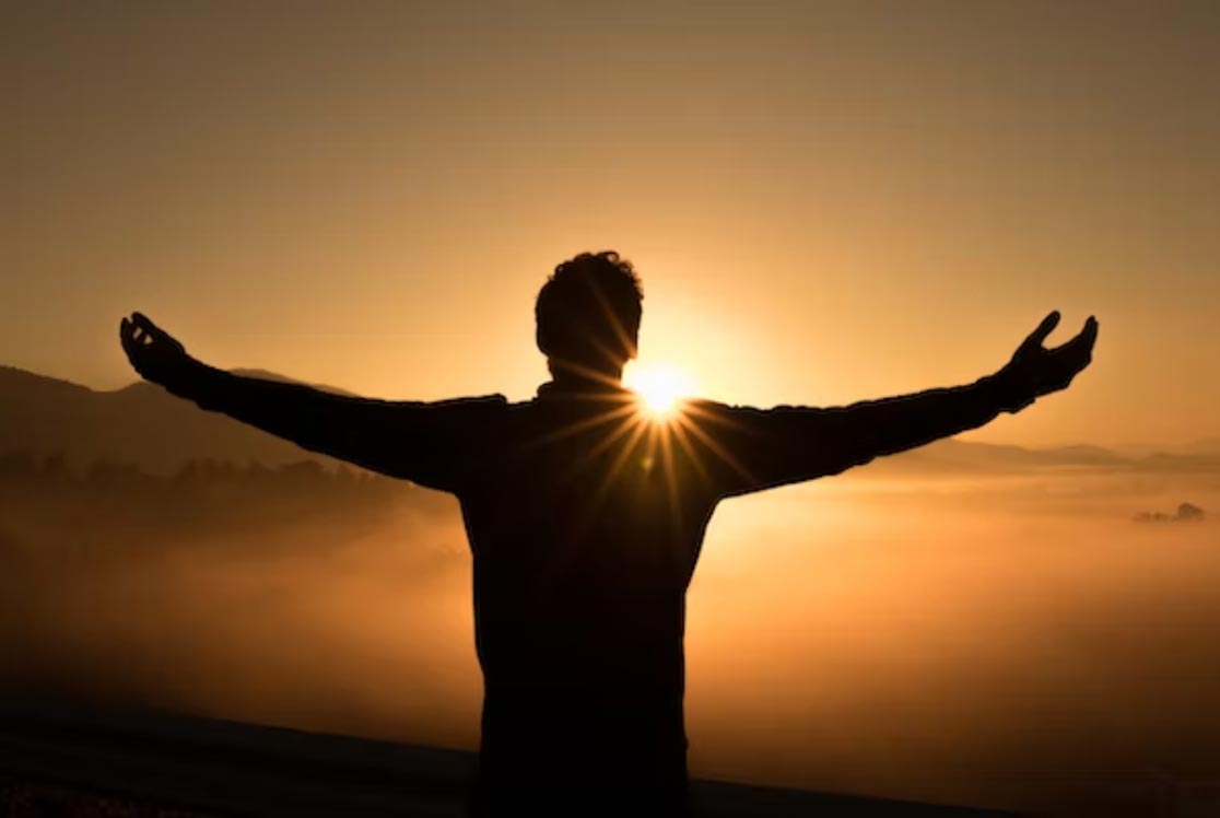 Man with outstretched arms toward a sunrise